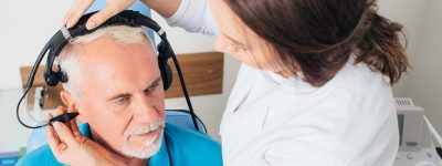Female doctor examining elderly patient ear , using special medical equipment, at doctors office